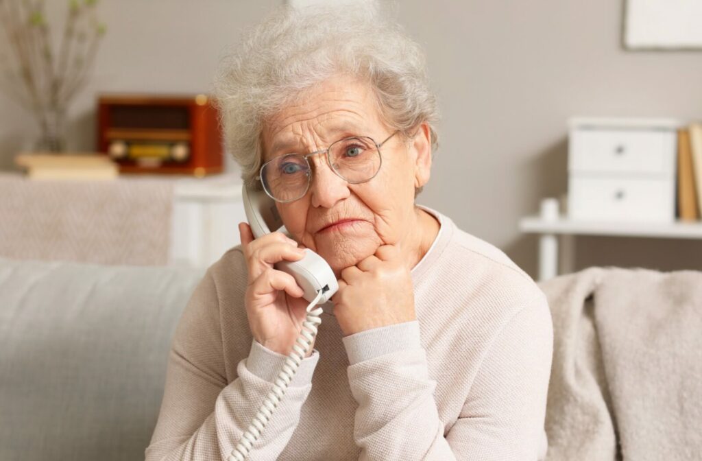 A melancholy senior rests her chin on her hand while on the phone.