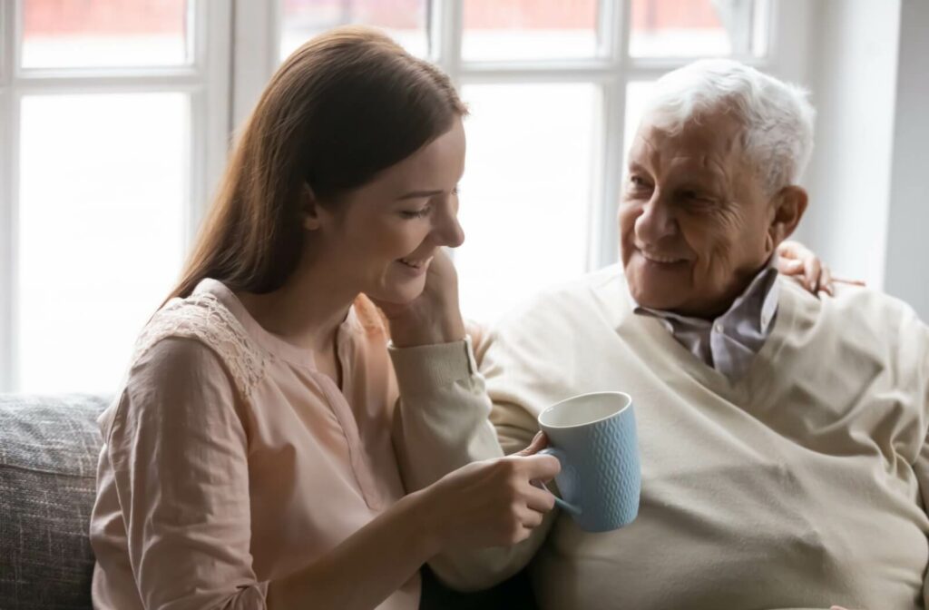 Smiling adult daughter sharing a warm moment with her elderly father, who is holding a mug.