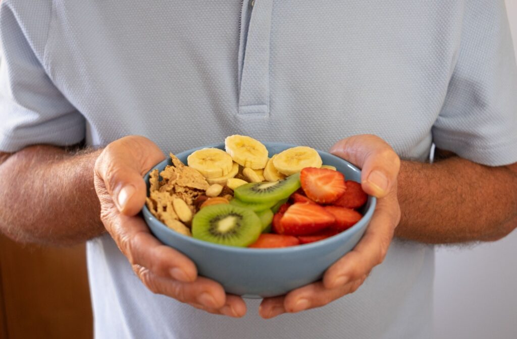 An adult holds a bowl full of sliced fruit and cereal as a balanced meal.